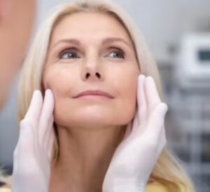 mujer mayor sujetandose la cara en evaluacion estetica en consulta con guantes blancos
